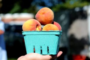 A person's hand holding a pint of peaches at the farmers market.