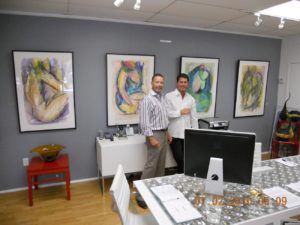 Two men in a gallery standing in front of artwork on the wall.