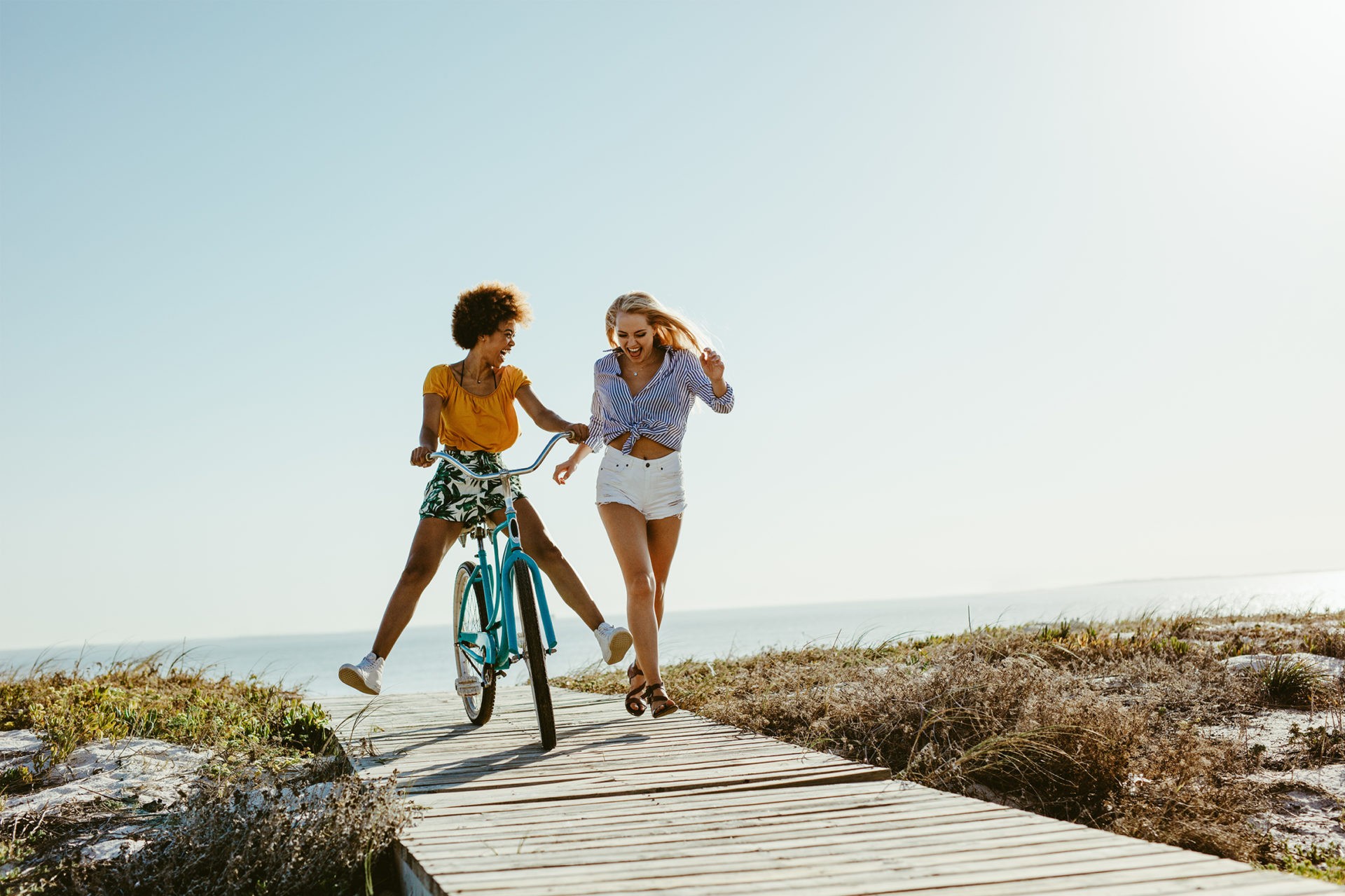 Two girls riding a bike and running at the beach.