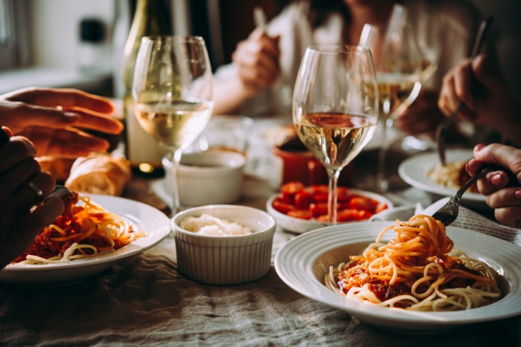 A group of people having an Italian dinner with wine and pasta at a restaurant.