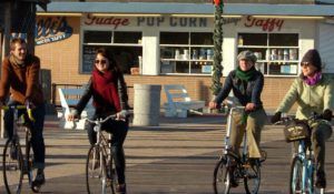 People riding bikes on boardwalk in front of candy store.