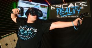 A person playing an arcade game wearing an escape reality shirt.